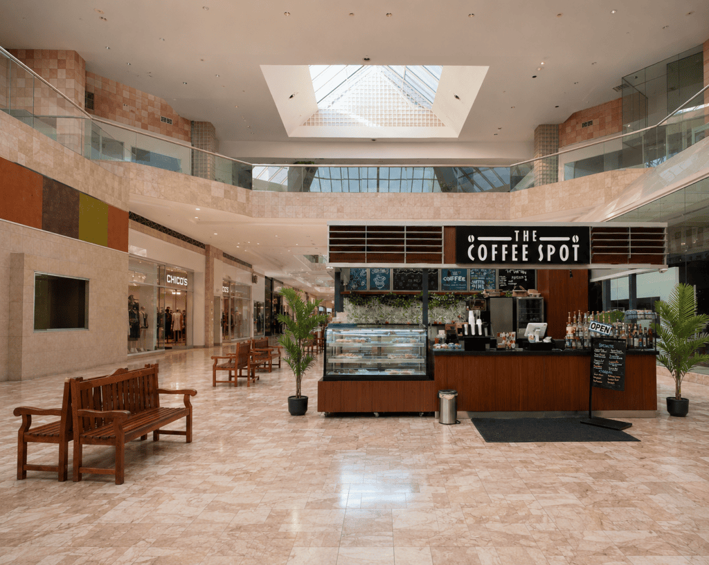 Southwestern shopping plaza with a white horse sculpture and a walk-up coffee kiosk under golden-hour light