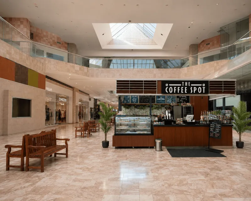 Southwestern shopping plaza with a white horse sculpture and a walk-up coffee kiosk under golden-hour light